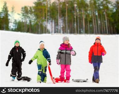 childhood, sledging and season concept - group of happy little kids with sleds in winter over forest background. happy little kids with sleds in winter