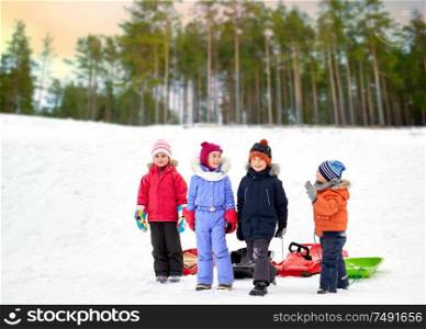 childhood, sledging and season concept - group of happy little kids with sleds over winter forest background. happy little kids with sleds in winter
