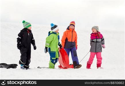 childhood, sledging and season concept - group of happy little kids with sleds outdoors in winter. happy little kids with sleds sledging in winter