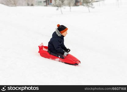 childhood, sledging and season concept - happy little boy sliding on sled down snow hill outdoors in winter. happy boy sliding on sled down snow hill in winter