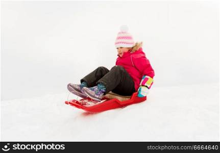 childhood, sledging and season concept - happy little girl sliding down on sled outdoors in winter. happy little girl sliding down on sled in winter