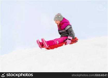 childhood, sledging and season concept - happy little girl sliding down on sled outdoors in winter. happy little girl sliding down on sled in winter