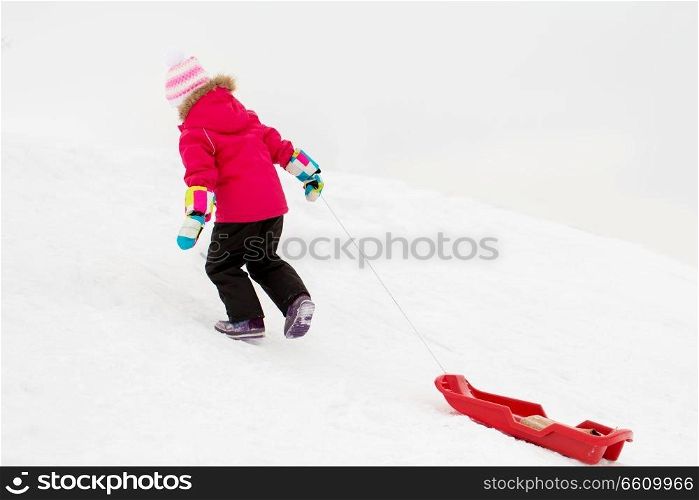 childhood, sledging and season concept - happy little girl with sled climbing snow hill in winter. little girl with sled on snow hill in winter