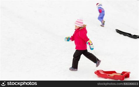 childhood, sledging and season concept - happy little girl with sleds climbing snow hill in winter. little girl with sleds on snow hill in winter