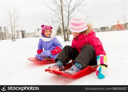 childhood, sledging and season concept - happy little girls on sleds outdoors in winter. happy little girls on sleds outdoors in winter