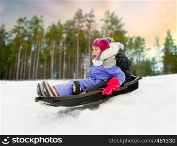 childhood, sledging and season concept - happy little kids sliding on sled down snow hill in winter over forest background. little kids sliding on sled down hill in winter