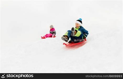 childhood, sledging and season concept - happy little kids sliding on sleds down snow hill in winter. happy kids sliding on sleds down hill in winter