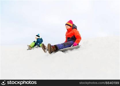 childhood, sledging and season concept - happy little kids sliding on sleds down snow hill in winter. happy kids sliding on sleds down hill in winter