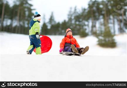 childhood, sledging and season concept - happy little kids sliding on sleds down snow hill in winter over snowy park or forest background. happy kids sliding on sleds down hill in winter