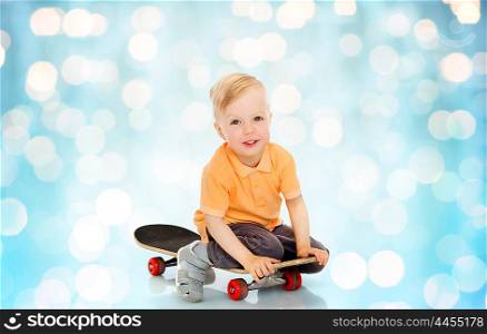 childhood, sport, leisure and people concept - happy little boy sitting on skateboard over blue holidays lights background