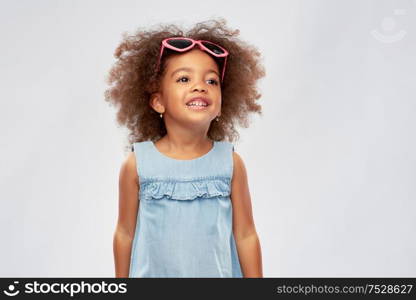 childhood, summer accessory and valentines day concept - happy little african american girl in heart shaped sunglasses over grey background. little african girl in heart shaped sunglasses