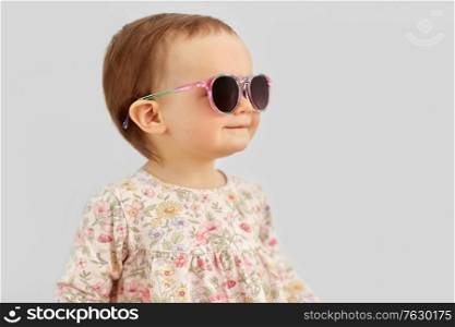 childhood, summer and people concept - happy little baby girl in sunglasses over grey background. happy little baby girl in sunglasses over grey