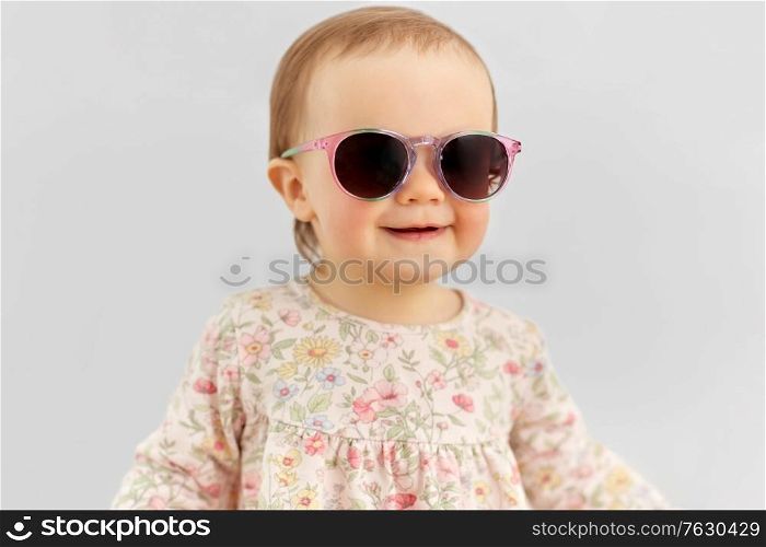 childhood, summer and people concept - happy little baby girl in sunglasses over grey background. happy little baby girl in sunglasses over grey