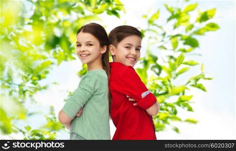 childhood, summer, and people concept - happy smiling boy and girl standing back to back over green natural background