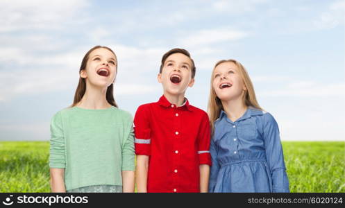 childhood, summer, emotion, friendship and people concept - happy amazed boy and girls looking up with open mouths over blue sky and grass background