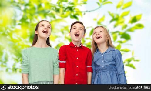 childhood, summer, emotion, friendship and people concept - happy amazed boy and girls looking up with open mouths over green natural background