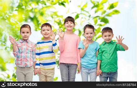 childhood, summer, fashion, friendship and people concept - group of happy smiling little children holding hands over green natural background