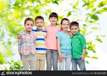 childhood, summer, fashion, friendship and people concept - group of happy smiling little children hugging over green natural background