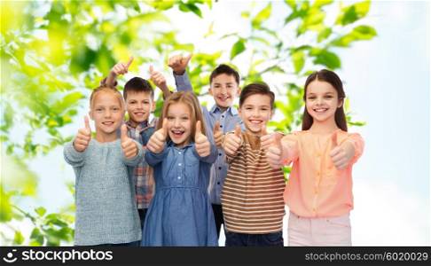 childhood, summer, gesture and people concept - happy smiling children showing thumbs up over green natural background