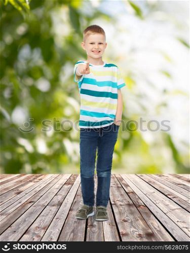 childhood, summer, gesture and people concept - smiling little boy pointing finger at you over plants and wooden floor background