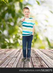 childhood, summer, gesture and people concept - smiling little boy pointing finger at you over plants and wooden floor background