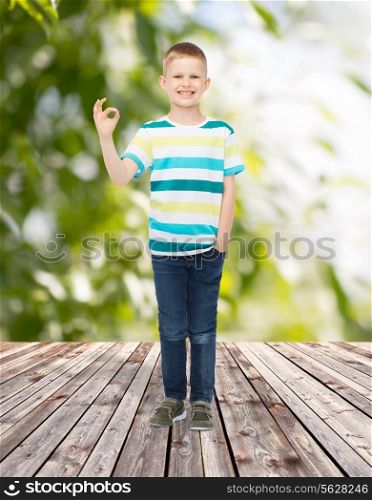 childhood, summer, gesture and people concept - smiling little boy showing ok sign over plants and wooden floor background