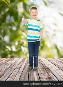 childhood, summer, gesture and people concept - smiling little boy showing thumbs up over plants and wooden floor background