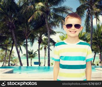 childhood, summer, travel, vacation and people concept - smiling little boy wearing sunglasses over pool and beach background