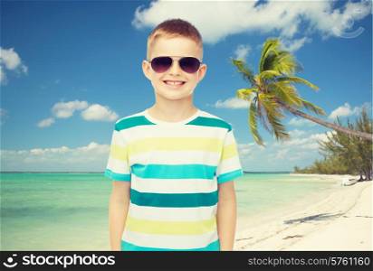 childhood, summer, travel, vacation and people concept - smiling little boy wearing sunglasses over beach background