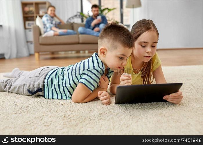 childhood, technology and family concept - brother and sister with tablet computer lying on floor at home. brother and sister with tablet computer at home