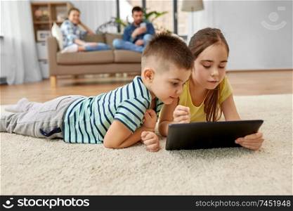 childhood, technology and family concept - brother and sister with tablet computer lying on floor at home. brother and sister with tablet computer at home