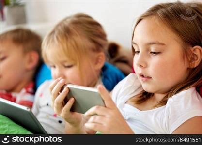 childhood, technology and family concept - little kids with smartphone and tablet pc computer in bed at home. little kids with smartphone in bed at home. little kids with smartphone in bed at home