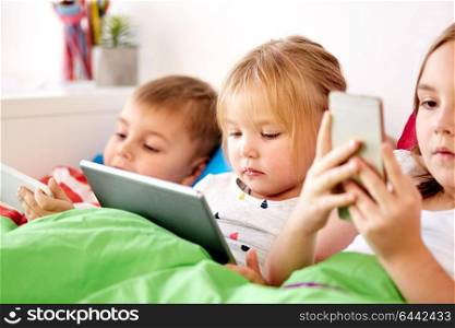 childhood, technology and family concept - little kids with tablet pc computer and smartphones in bed at home. little kids with tablet pc in bed at home