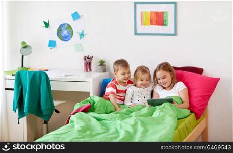 childhood, technology and family concept - little kids with tablet pc computer in bed at home. little kids with tablet pc in bed at home