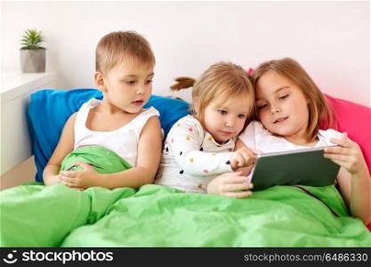 childhood, technology and family concept - little kids with tablet pc computer in bed at home. little kids with tablet pc in bed at home. little kids with tablet pc in bed at home