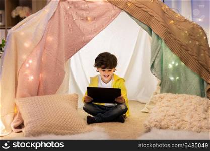 childhood, technology and hygge concept - happy little boy with tablet pc computer in kids tent at home. little boy with tablet pc in kids tent at home. little boy with tablet pc in kids tent at home