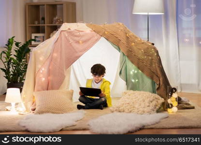 childhood, technology and hygge concept - happy little boy with tablet pc computer in kids tent at home. little boy with tablet pc in kids tent at home. little boy with tablet pc in kids tent at home