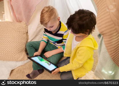 childhood, technology and hygge concept - happy little boys with tablet pc computer in kids tent at home. little boys with tablet pc in kids tent at home. little boys with tablet pc in kids tent at home