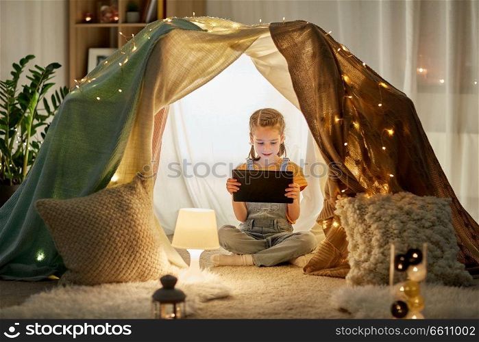 childhood, technology and hygge concept - happy little girl with tablet pc computer in kids tent at home. little girl with tablet pc in kids tent at home