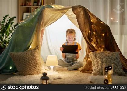 childhood, technology and hygge concept - happy little girl with tablet pc computer in kids tent at home. little girl with tablet pc in kids tent at home