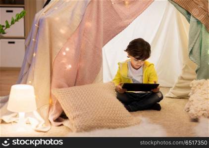 childhood, technology and hygge concept - little boy with tablet pc computer in kids tent at home. little boy with tablet pc in kids tent at home. little boy with tablet pc in kids tent at home