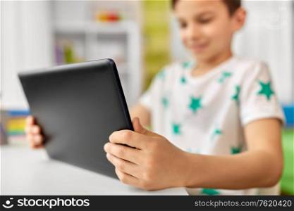 childhood, technology and people concept - close up of boy with tablet pc computer sitting at table. close up of boy with tablet pc sitting at table