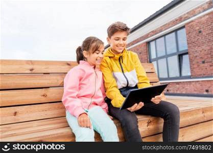 childhood, technology and people concept - happy children or brother and sister with tablet computer sitting on wooden street bench outdoors. children with tablet computer sitting on bench