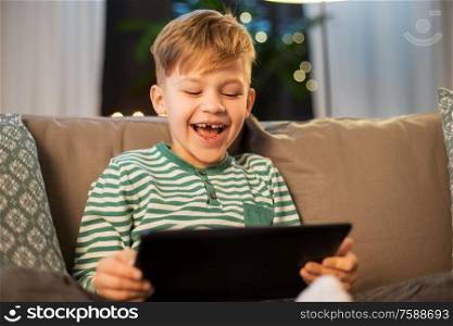 childhood, technology and people concept - happy smiling little boy with tablet pc computer at home in evening. happy little boy with tablet computer at home