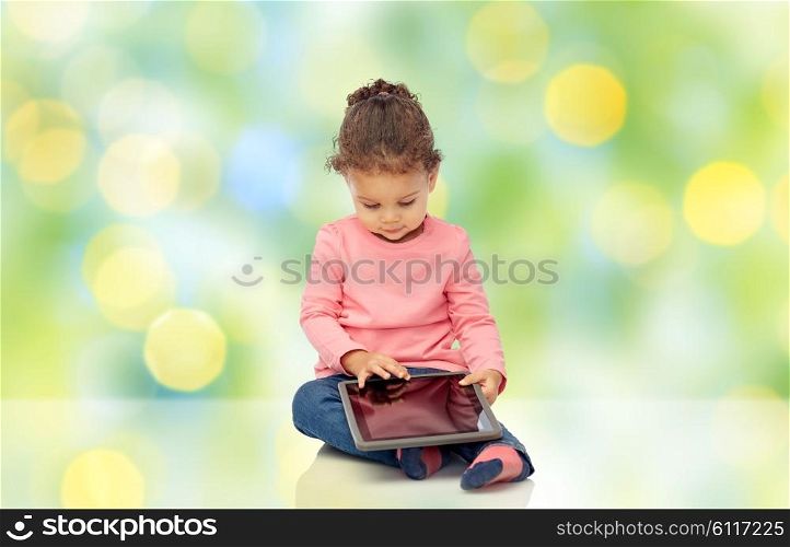childhood, technology and people concept - little african american baby girl playing with tablet pc computer and sitting on floor