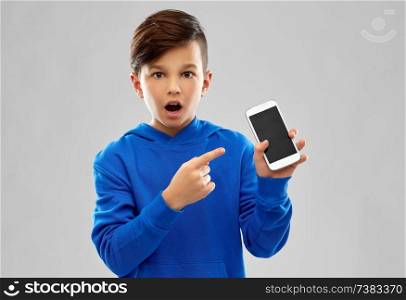 childhood, technology and people concept - shocked boy in blue hoodie showing smartphone with blank screen over grey background. shocked boy in blue hoodie showing smartphone
