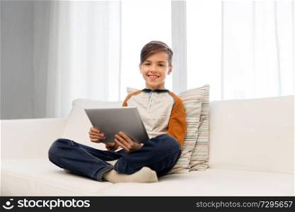 childhood, technology and people concept - smiling boy with tablet pc computer sitting on sofa at home. smiling boy with tablet pc computer at home