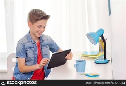 childhood, technology and people concept - smiling boy with tablet pc computer sitting at home desk. smiling boy with tablet pc sitting at home desk