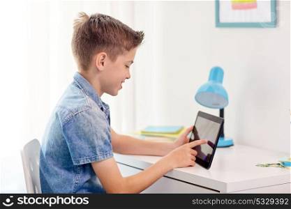 childhood, technology and people concept - smiling boy with tablet pc computer sitting at home desk. smiling boy with tablet pc sitting at home desk