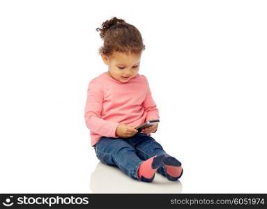 childhood, technology and people concept - smiling little african american baby girl playing with smartphone and sitting on floor